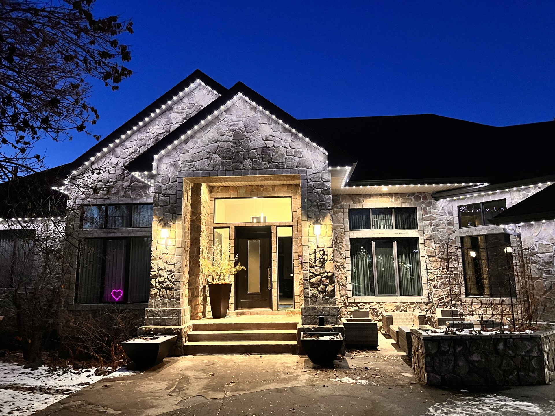 Crisp white permanent LED lights on stone facade home at dusk